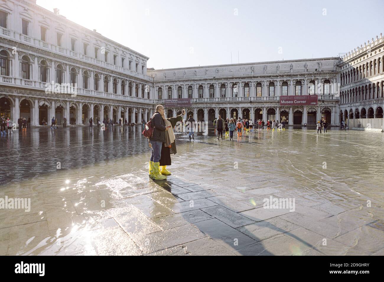 Turisti che scattano fotografie in Piazza San Marco con alta marea, acqua alta, con vista sulla San Marco Procuratie Foto Stock