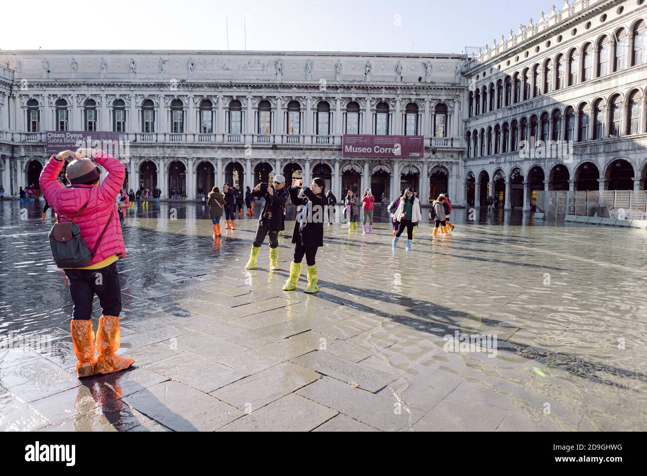 Turisti che scattano fotografie in Piazza San Marco con alta marea, acqua alta, con vista sulla San Marco Procuratie Foto Stock