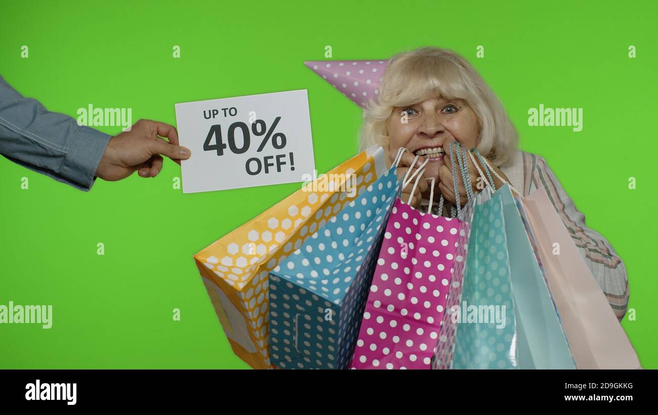 Iscrizione fino al 40% di sconto appare accanto alla nonna sorridente. Donna anziana con borse per la spesa festeggiando, ballando, cercando soddisfatto con prezzi bassi, sconti, shopping su Black Friday Foto Stock