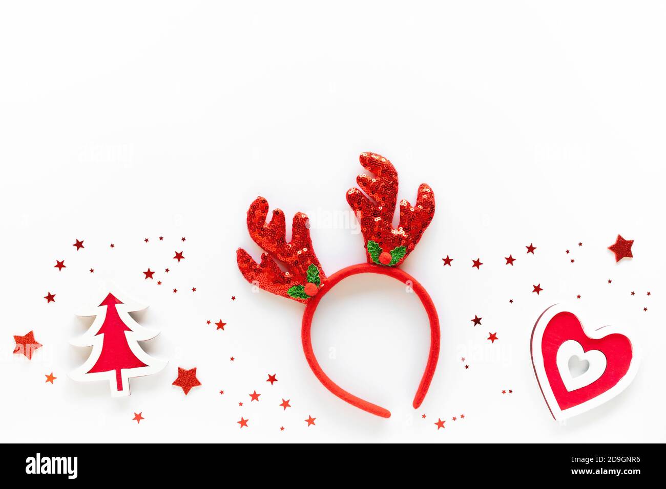 Composizione d'arte natalizia con decorazioni rosse, archetto in renna su superficie bianca. Concetto di festa di Natale. Disposizione piatta, spazio per la copia, biglietto d'auguri Foto Stock