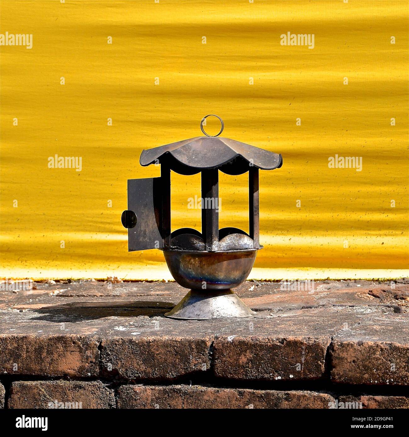 Vista ravvicinata di una lanterna arrugginita su una base di mattoni, sullo sfondo di un tessuto giallo del tempio in un tempio buddista. Foto Stock