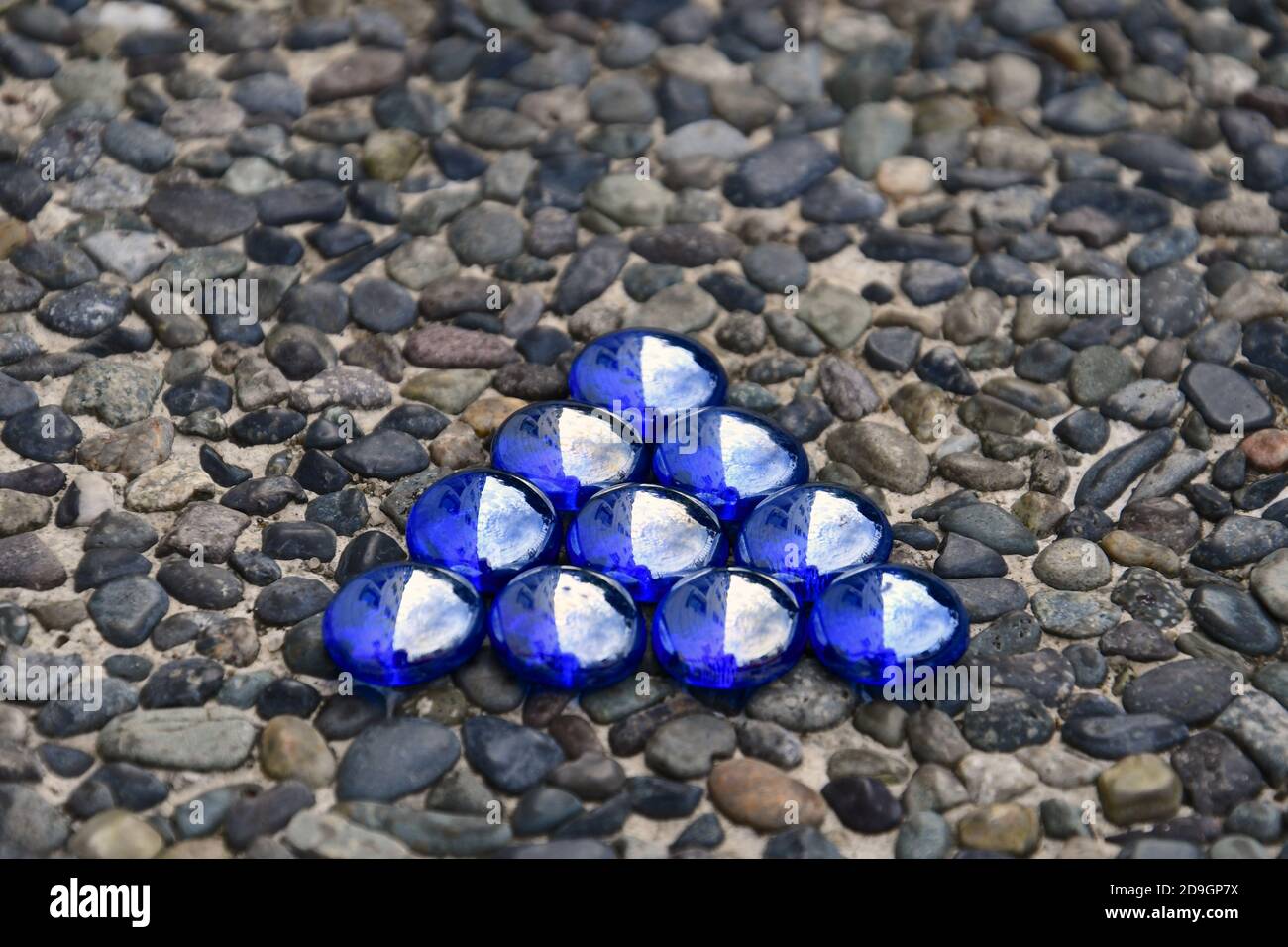 Triangolo di perline di vetro blu iridescenti isolato su uno sfondo di pietra ciottolosa. Foto Stock