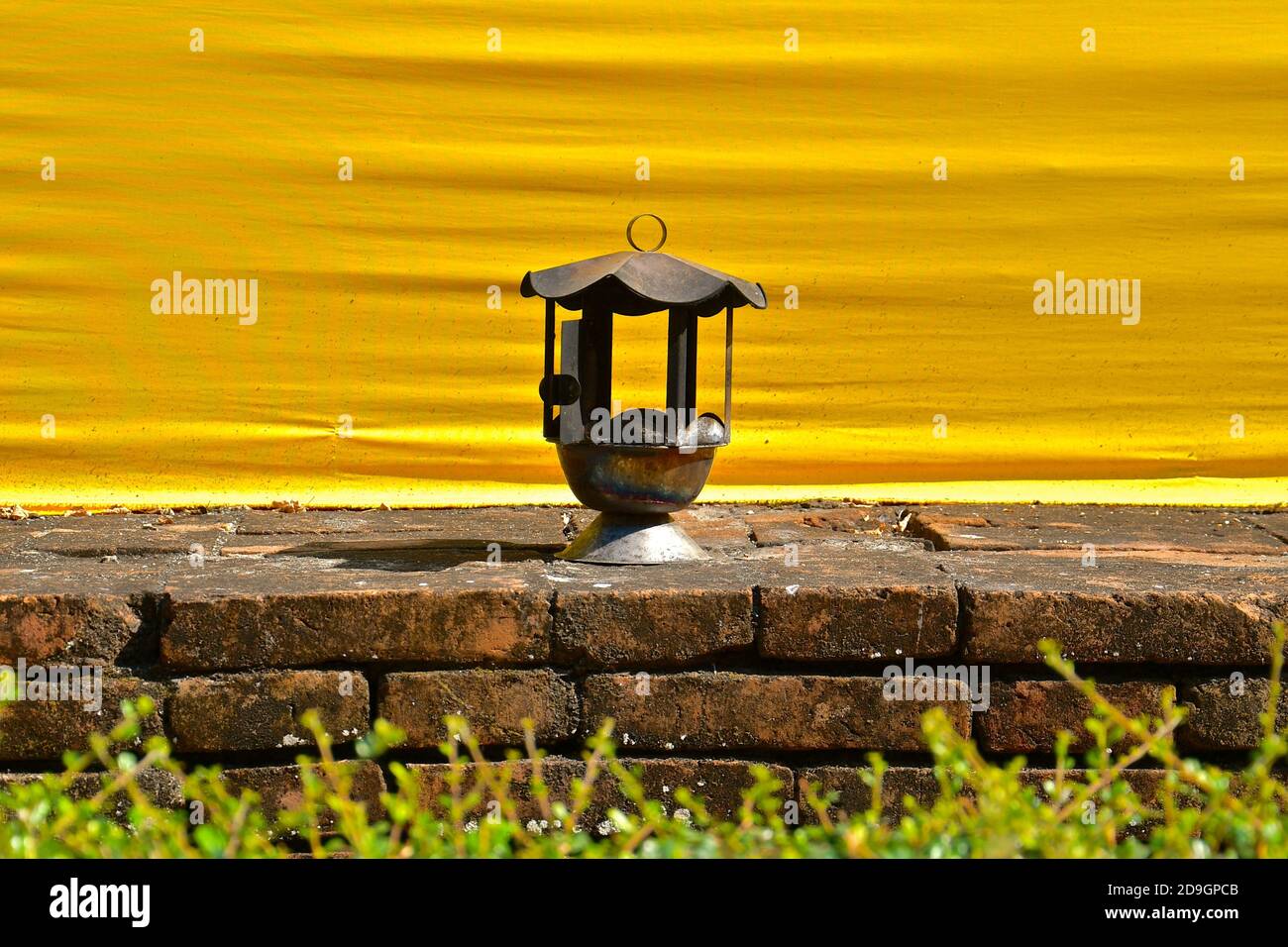 Vista ravvicinata di una lanterna arrugginita su una base di mattoni, sullo sfondo di un tessuto giallo del tempio in un tempio buddista. Foto Stock