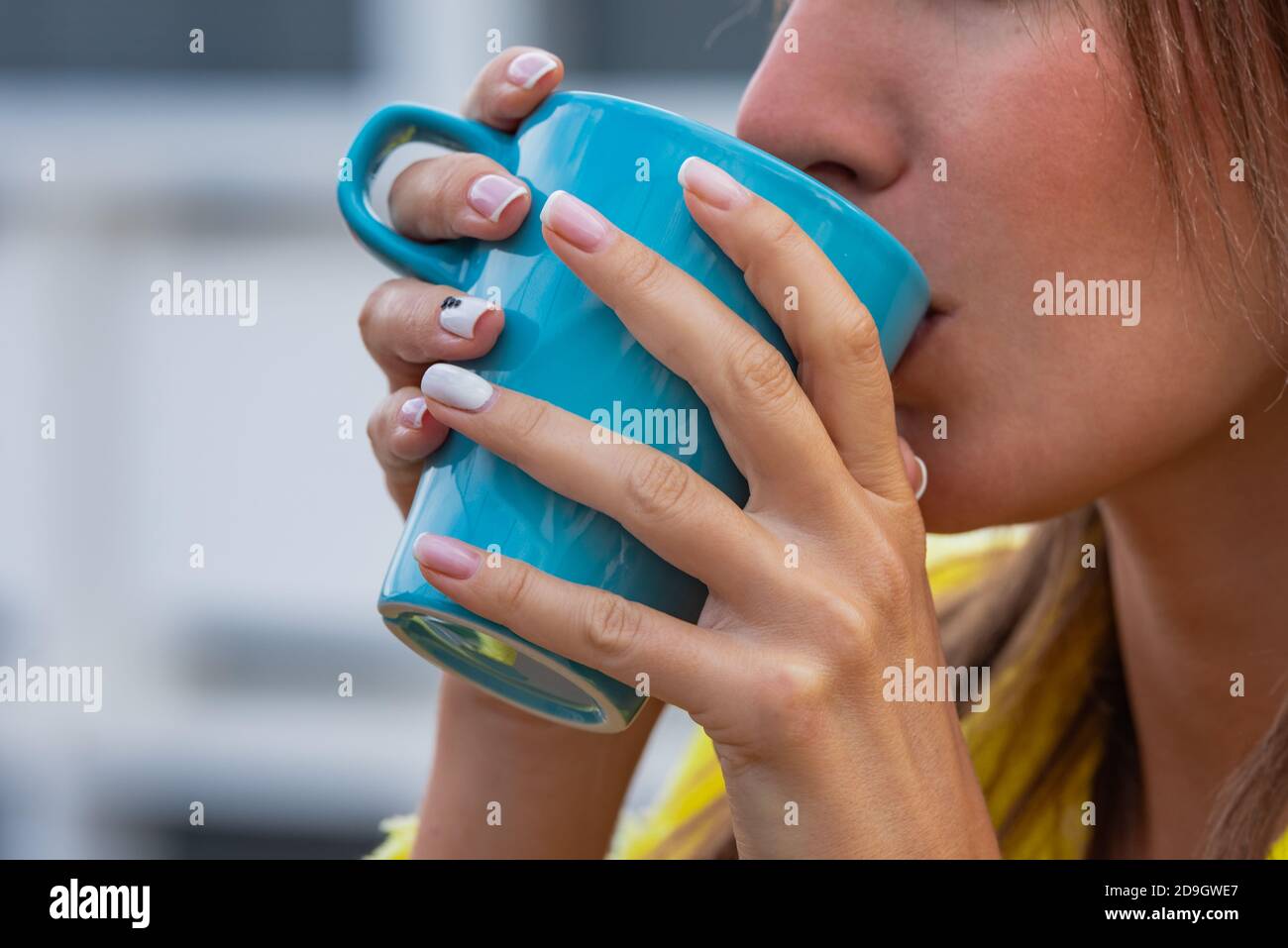 Giovane donna che beve tè o caffè verme da una tazza blu. Foto Stock