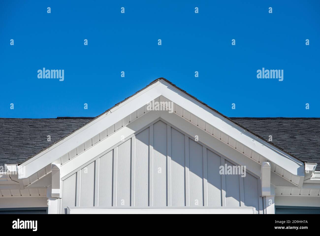 A forma di triangolo decorativo gable con soffit coloniale bianco e fascia su un blu grigio orizzontale vinile che sorsegge la moderna casa americana della tenuta Foto Stock