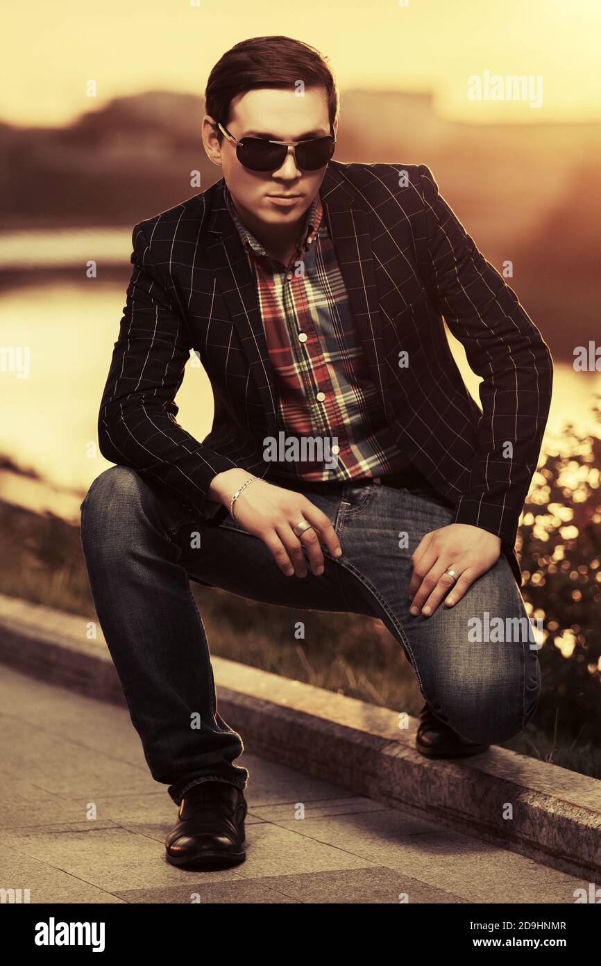 Giovane bel uomo d'affari in occhiali da sole sulla città strada elegante modello di moda maschile in nero blazer e jeans blu scuro Foto Stock
