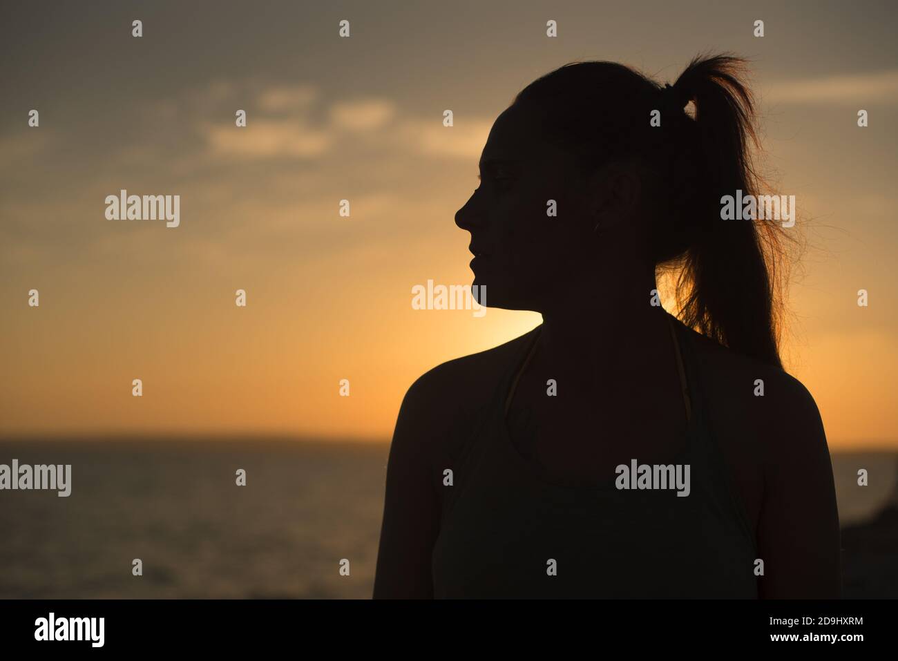 Profilo retroilluminato di una bella donna che guarda un bel tramonto sul mare. Primo piano. Isola di Formentera, Spagna. Foto Stock