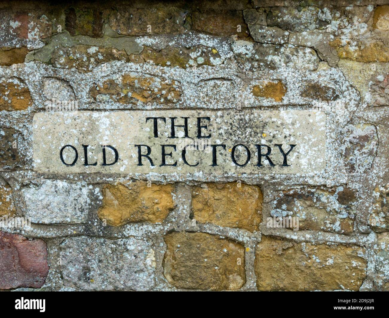 Closeup di 'la vecchia canonica' scolpito casa segno con lettere nere set in vecchio rustico muro di ironstone, Cnossington, Leicestershire, Inghilterra, Regno Unito Foto Stock