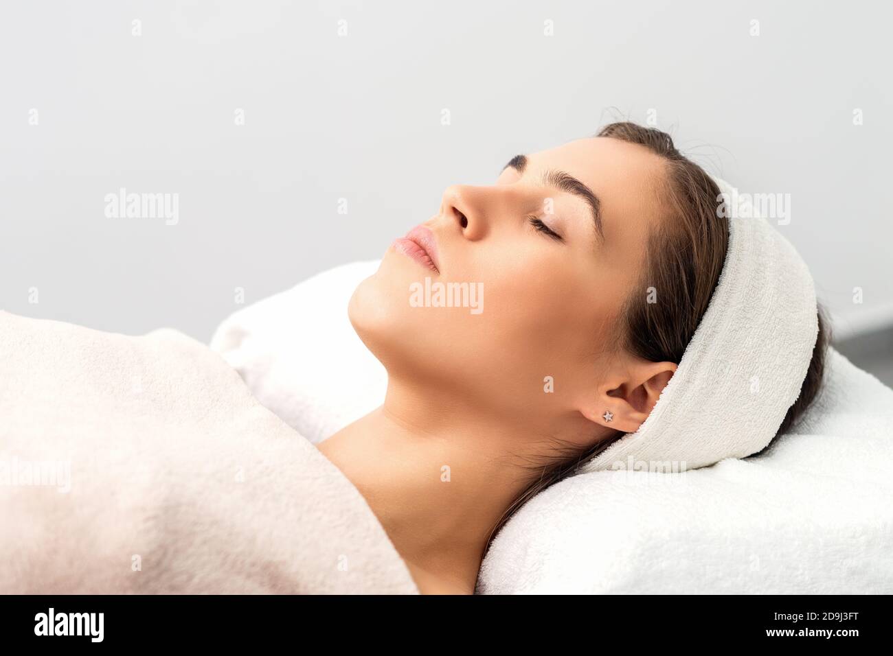Vista laterale di giovane donna sdraiata su tavolo estetista con occhi chiusi in attesa di una procedura cosmetica in salone di bellezza Foto Stock