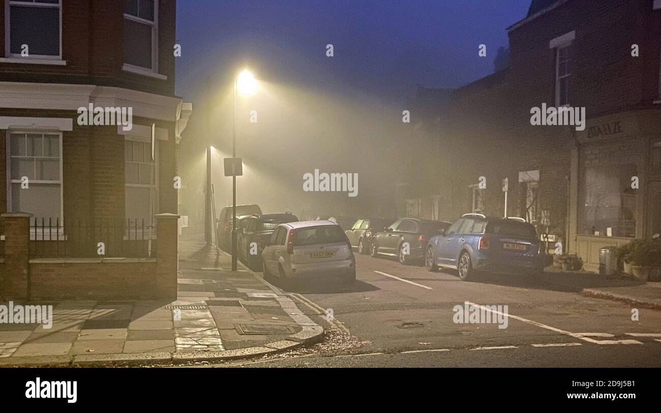 I lampioni illuminano le auto parcheggiate attraverso la nebbia in una strada a Kew, a ovest di Londra. I previsori si aspettano che le condizioni avverse si sollevino più tardi al mattino, prima di tornare questa sera. Foto Stock