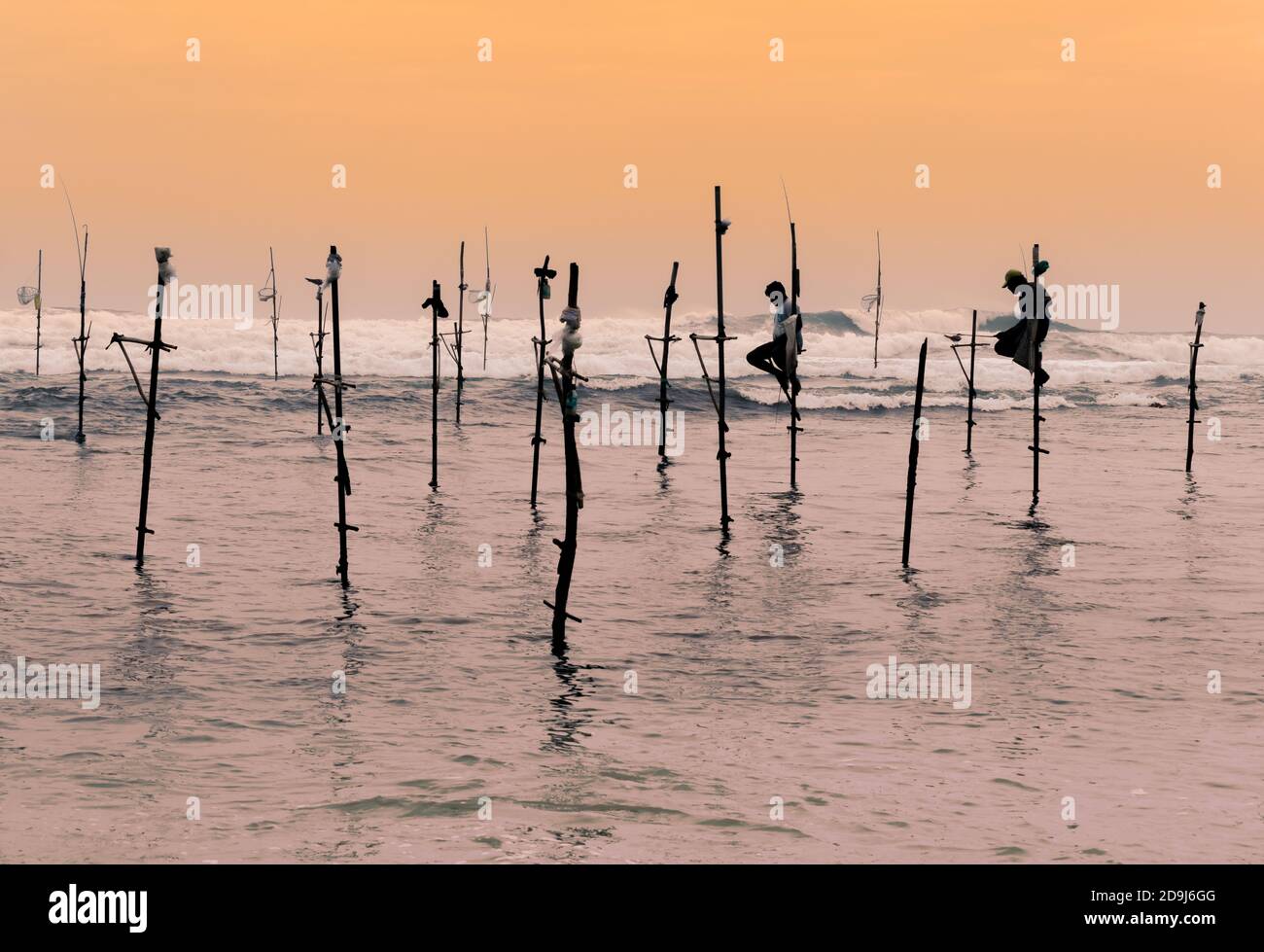 Un paio di pescatori di Swilt seduti sui loro pali con canne da pesca in legno nelle loro mani nella sera del tramonto. Le onde oceaniche si schiantano dietro di loro nel Foto Stock