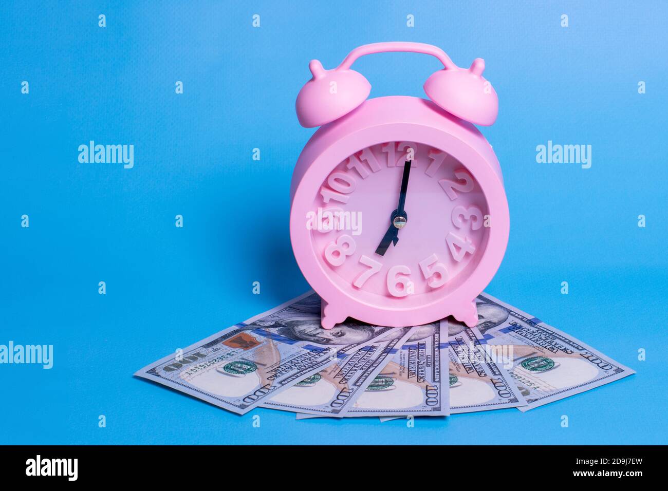 Il concetto di accumulo di denaro. Alzati al lavoro per fare soldi. Attività femminile. Denaro e sveglia rosa isolati su sfondo blu. Foto Stock