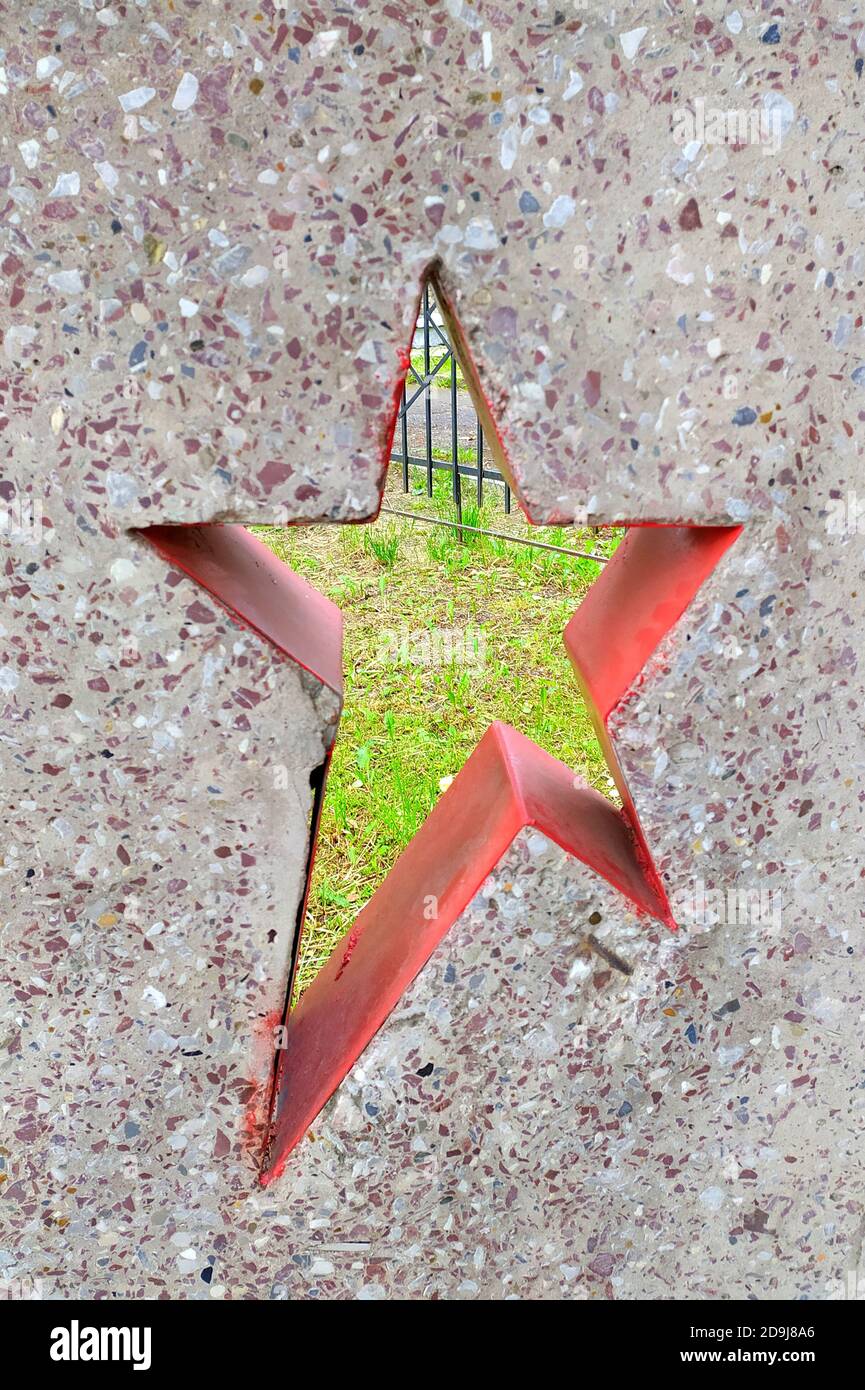 Parete in cemento con un foro a forma di stella a cinque punte di colore rosso. Il foro mostra l'erba verde. Frammento del monumento alle truppe sovietiche. Memoriale in Russia a coloro che sono morti durante la seconda guerra mondiale o la guerra civile russa. Foto Stock
