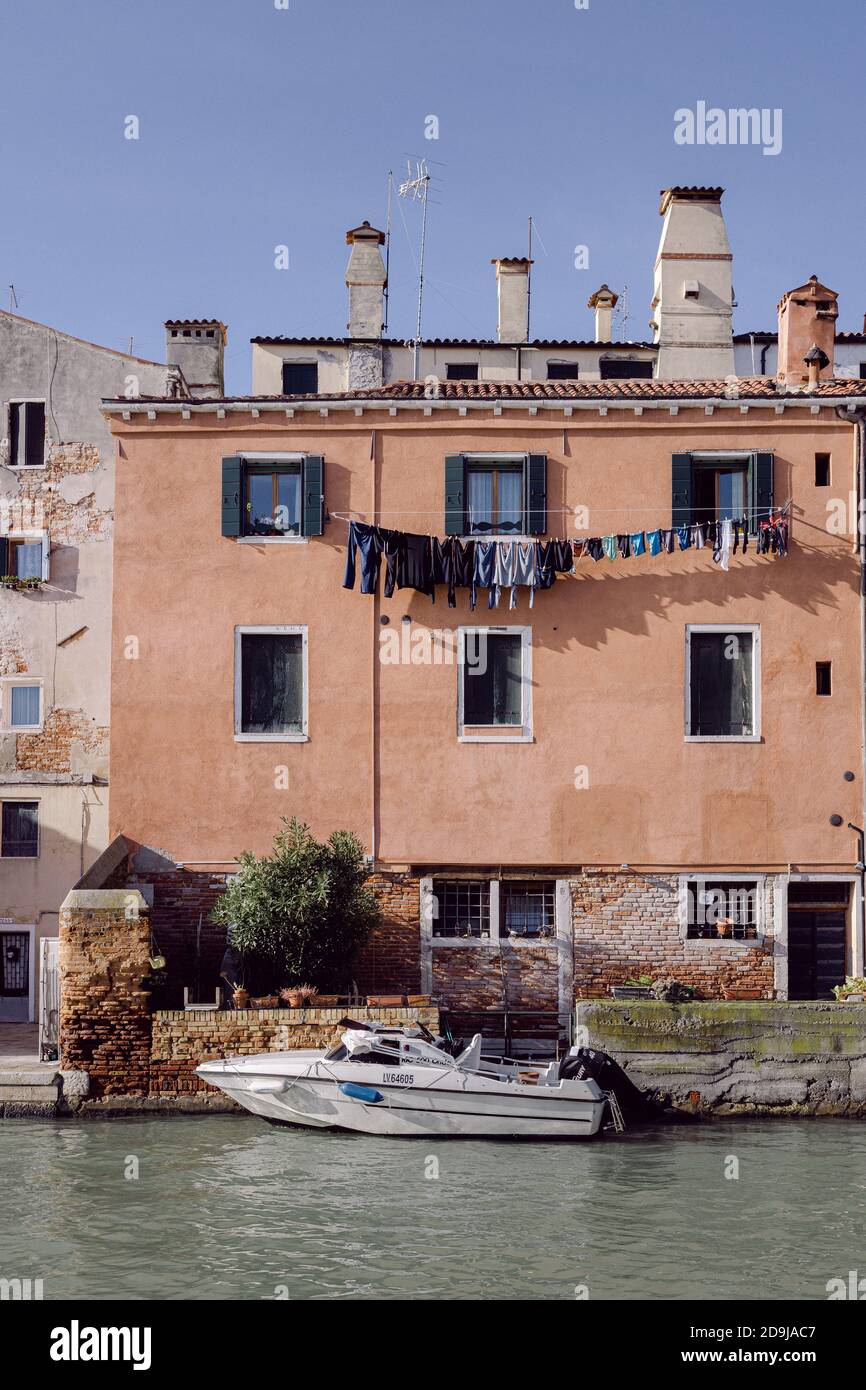 Alto edificio esterno con parete arancione, barca ormeggiata su un canale di Venezia Foto Stock