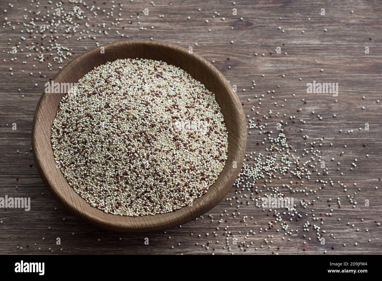 Quinoa crude mescolate in ciotola di legno su tavola di legno. Supercibo sano e senza glutine Foto Stock