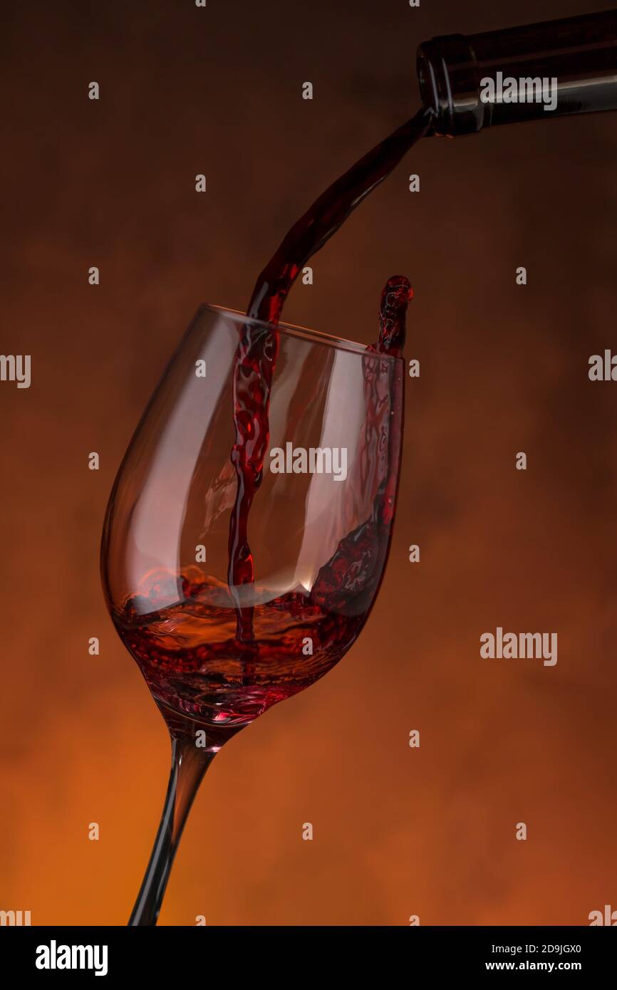 Bottiglia che riempie un bicchiere di vino rosso su fondo rossastro Foto Stock
