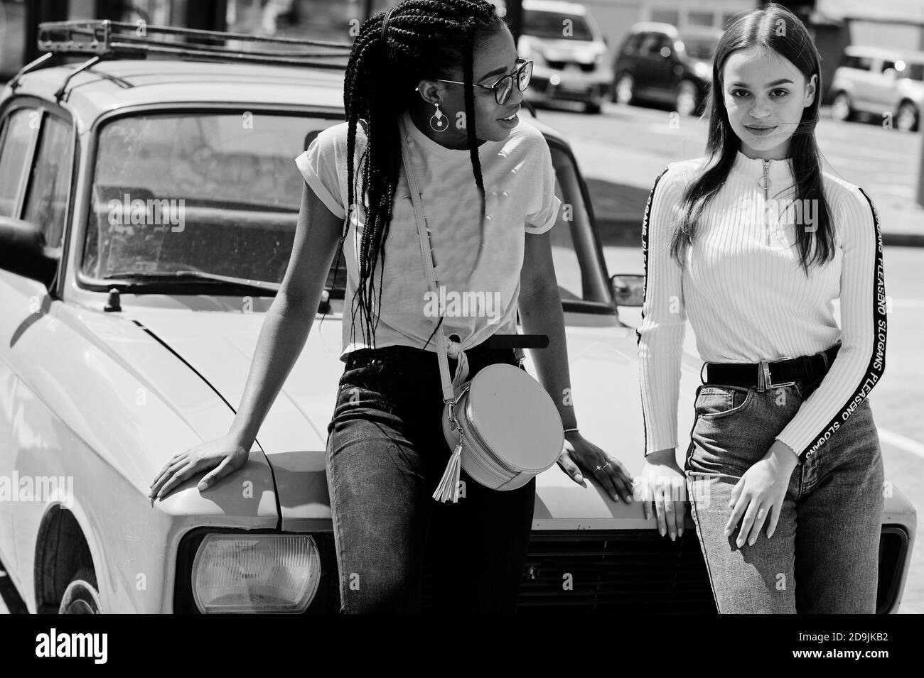 Bianca caucasica ragazza e nero afroamericano insieme contro vecchia auto retrò. L'unità del mondo, l'amore razziale, la comprensione nella tolleranza e le razze diversi Foto Stock