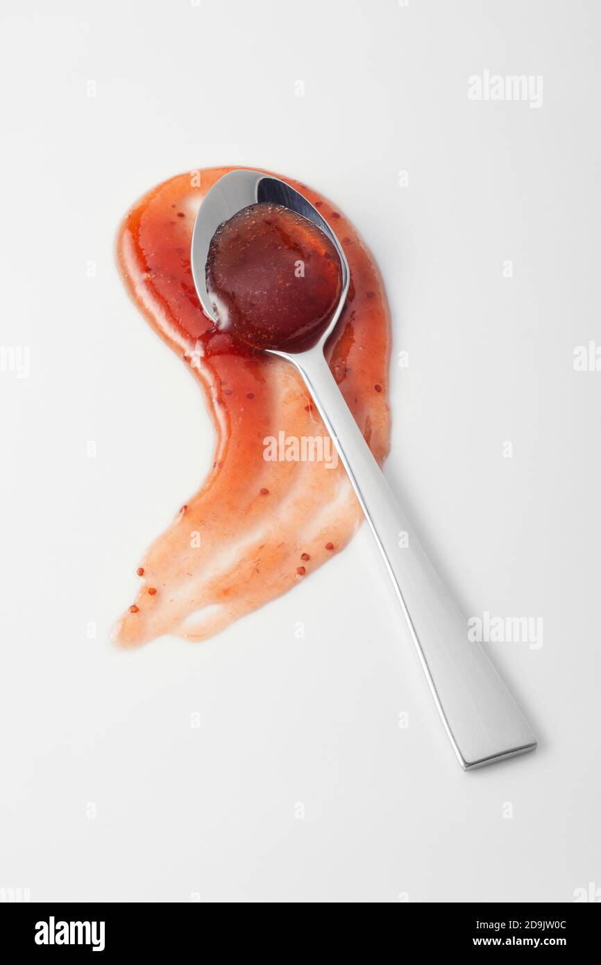 Deliziosa salsa di marmellata rossa piccante su bianco in una cucchiaio d'argento su un blob curvante per la pubblicità Foto Stock