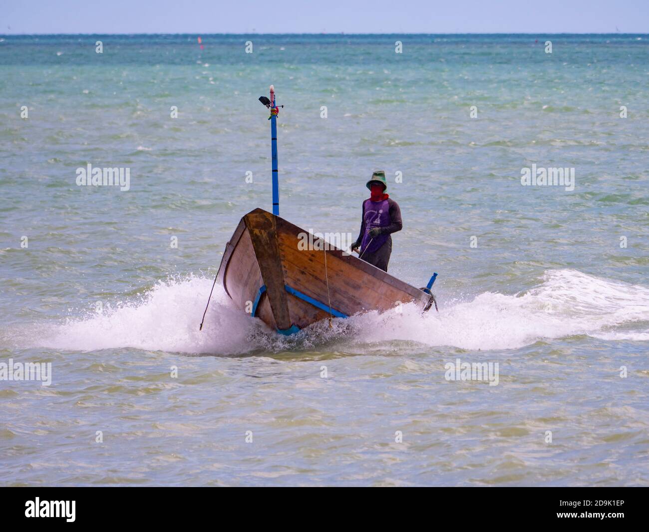 Pescatore che arriva al porto sulla sua tradizionale barca di legno dopo una giornata piovosa in mare nella provincia di Rayong in Thailandia. Foto Stock