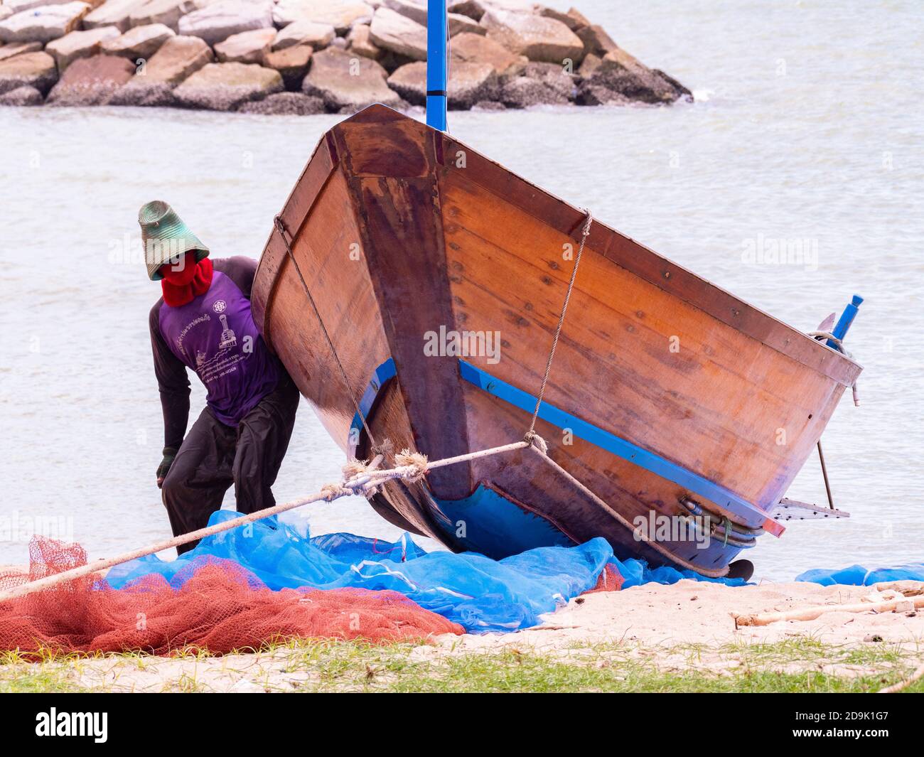 Pescatore che trasporta la sua tradizionale barca di legno sulla spiaggia dopo una giornata piovosa in mare nella provincia di Rayong in Thailandia. Foto Stock