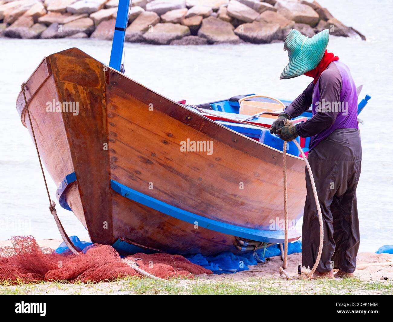 Pescatore che lavora sulla sua tradizionale barca di legno dopo una giornata piovosa in mare nella provincia di Rayong in Thailandia. Foto Stock