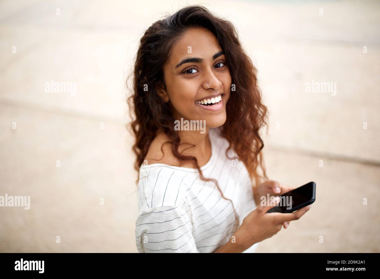 Primo piano ritratto sorridente giovane donna indiana che tiene il telefono cellulare esterno Foto Stock