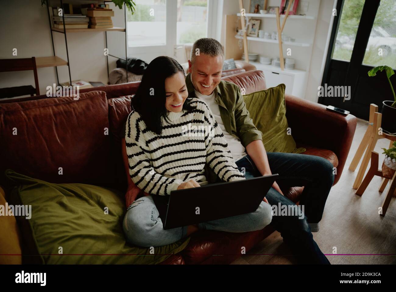 Vista ad alto angolo di una giovane coppia sorridente seduta insieme divano con computer portatile Foto Stock