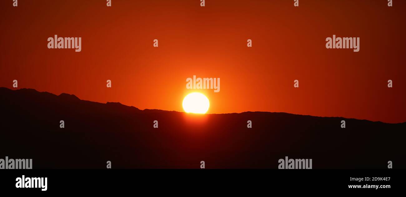 Bella Alba sulle montagne contorno delle montagne, alba arancione. Disco del sole e i primi raggi del sole Foto Stock