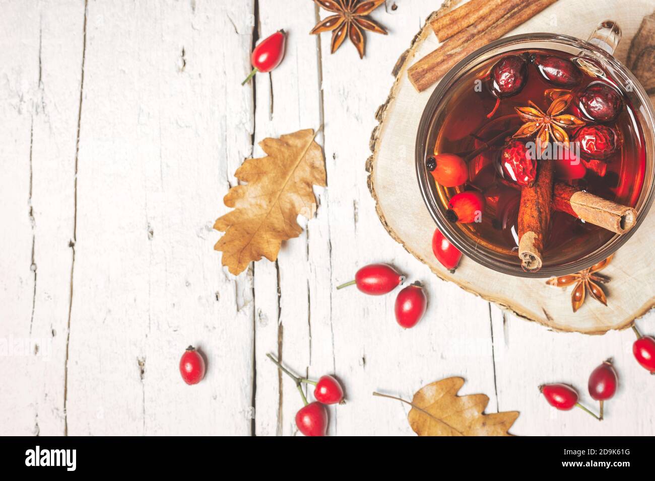 Foto ravvicinata di una tazza di tè con fianchi di rose, spezie e foglie essiccate su rustico sfondo in legno, vista dall'alto. Bevanda vitaminica autunnale. Foto Stock