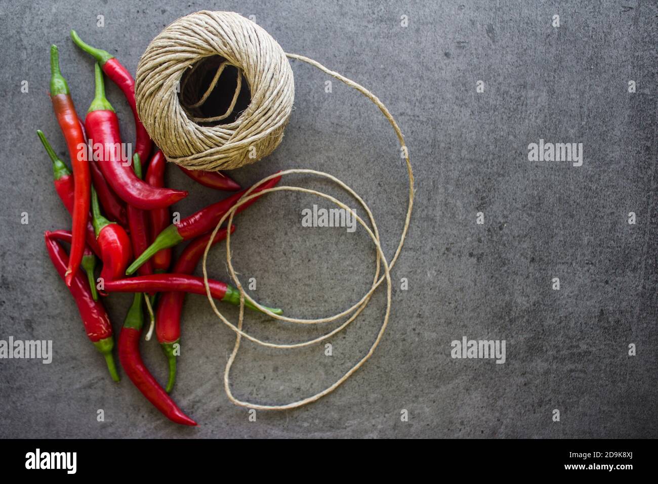 Preparare la ghirlanda di peperoncini rossi. Peperoni freschi e corda di lino su tavolo grigio scuro. Foto vista dall'alto con spazio per la copia. Decorazioni fatte a mano a casa. Foto Stock