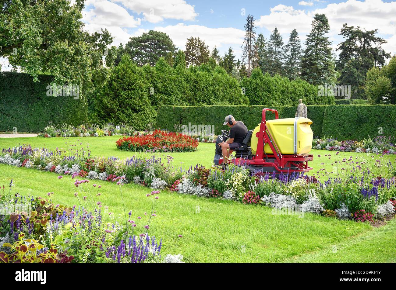 L'uomo taglia l'erba nel giardino fiorito del castello di Lednice guidando la macchina falciante in giornata di sole Foto Stock