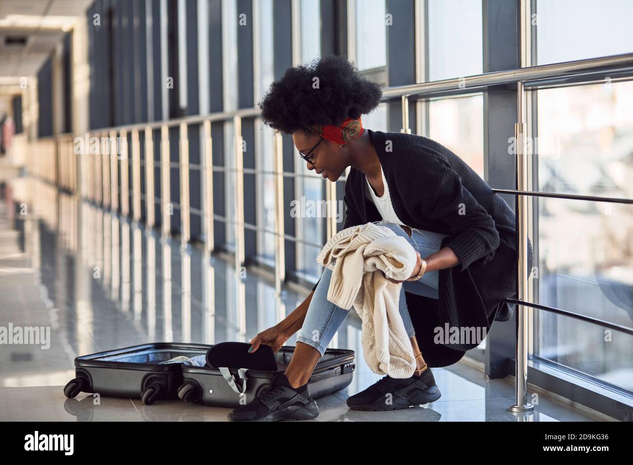 Giovane donna afro-americana in abbigliamento casual è in aeroporto con i vestiti di imballaggio del bagaglio Foto Stock