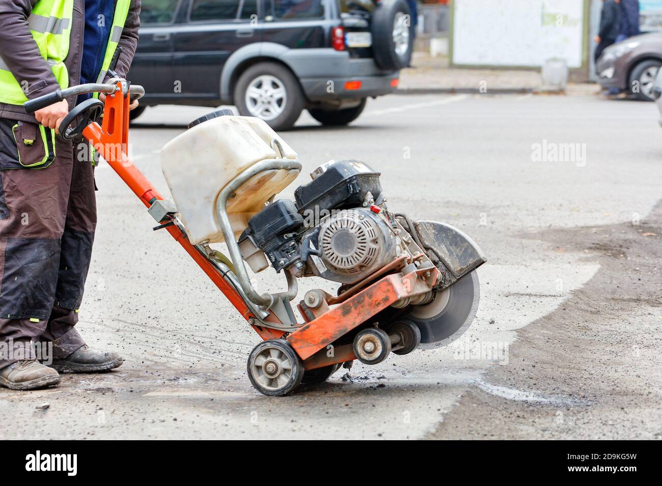 Un lavoratore sposta una taglierina a benzina con una ruota di taglio diamantata funzionante su una sezione difettosa della strada che deve essere riparata. Foto Stock