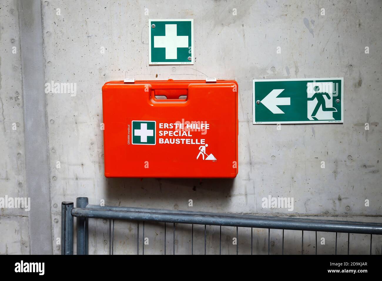 Renania Settentrionale-Vestfalia, Germania, kit di pronto soccorso su una parete di cemento accanto a un cartello di uscita di emergenza su un cantiere, immagine simbolica della sicurezza sul lavoro. Foto Stock