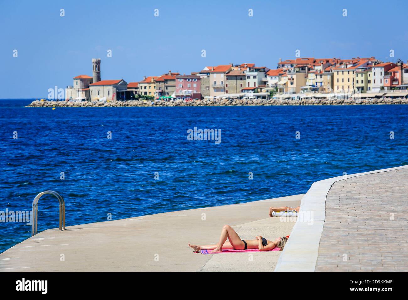 Piran, Istria, Slovenia - bagnanti sulla spiaggia della città di cemento Fornace della città portuale di Piran sul Mar Mediterraneo. Foto Stock