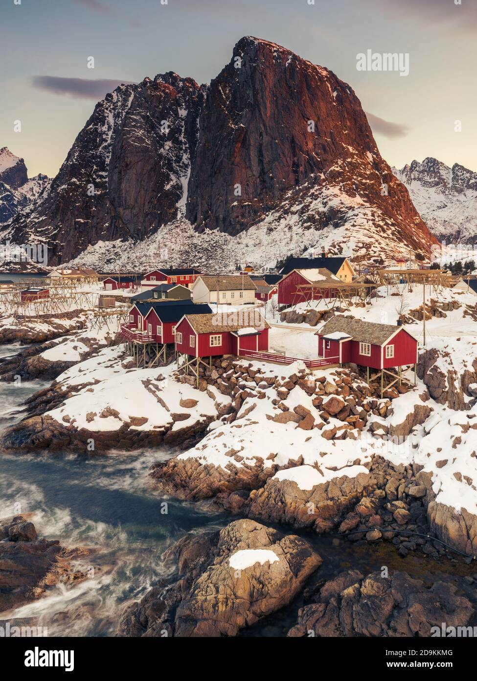 Iconiche case in palafitte rosse sulla costa del villaggio Hamnøy sulle isole Lofoten in Norvegia in inverno limpido mattina con montagna ripida ricoperta di neve Foto Stock