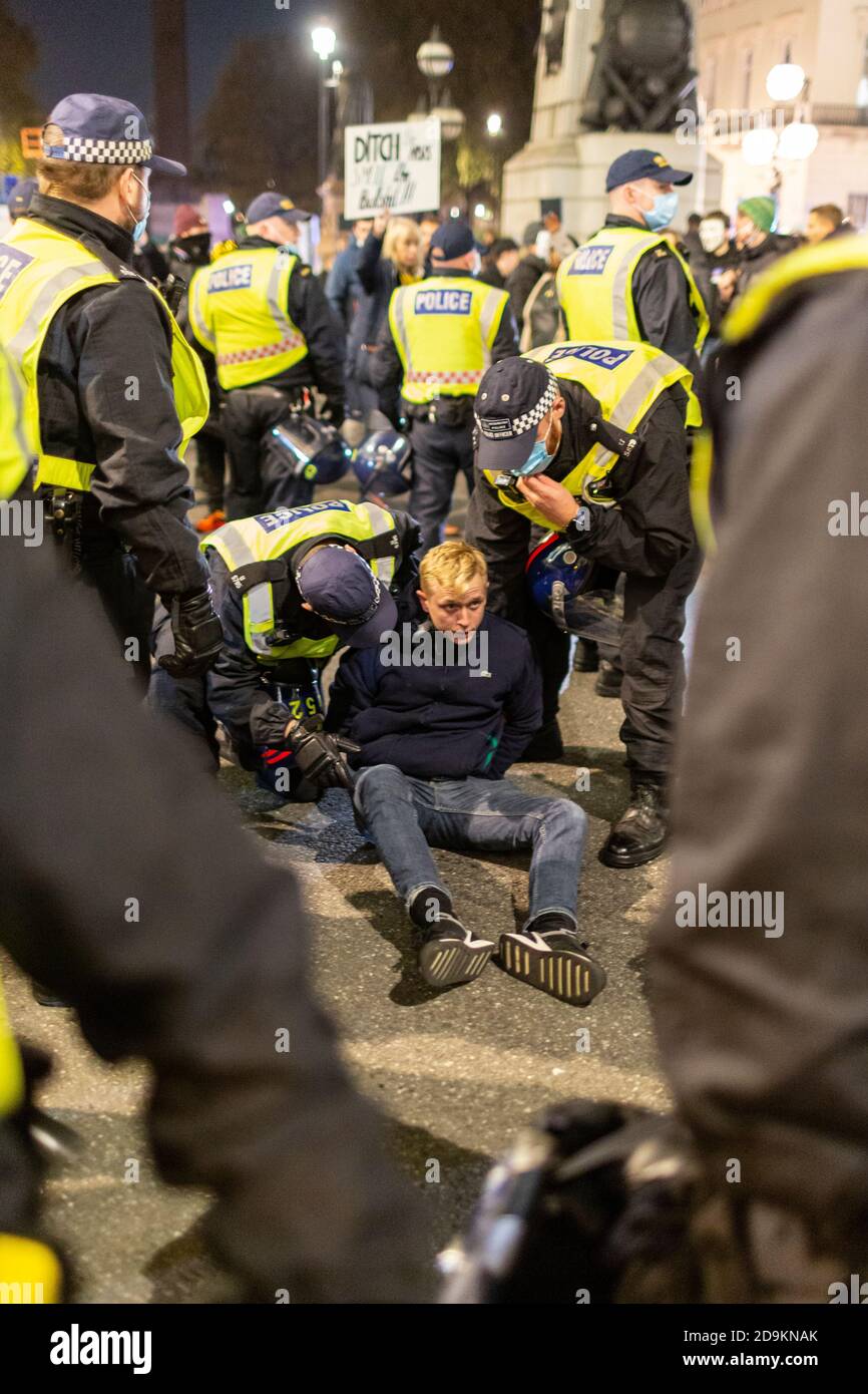 Un protestante arrestato si siede sulla strada circondata dalla polizia durante la Million Mask March cui hanno partecipato molti scettici di blocco, Londra, 5 novembre 2020 Foto Stock