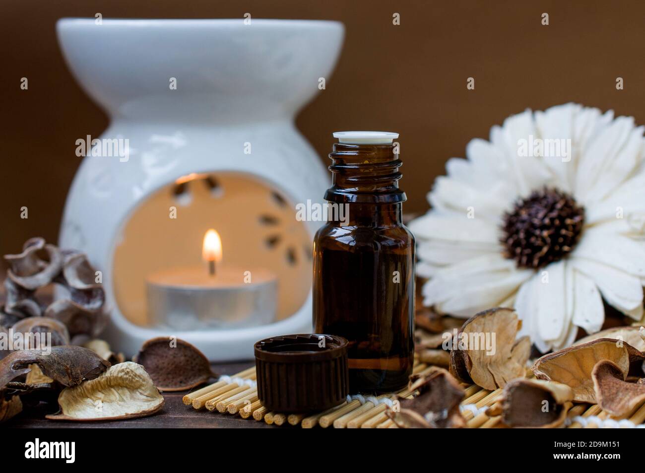 Lampada aromatica con candela bruciante, bottiglia di olio aromatico, in tonalità marrone, decorata con un fiore. Relax e atmosfera termale. Aromaterapia Foto Stock