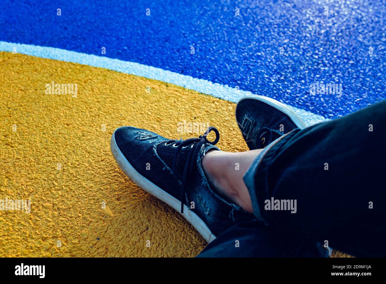 Vista dall'alto delle gambe femminili accanto alla linea bianca curva su sfondo giallo blu. Concetto di separazione Foto Stock