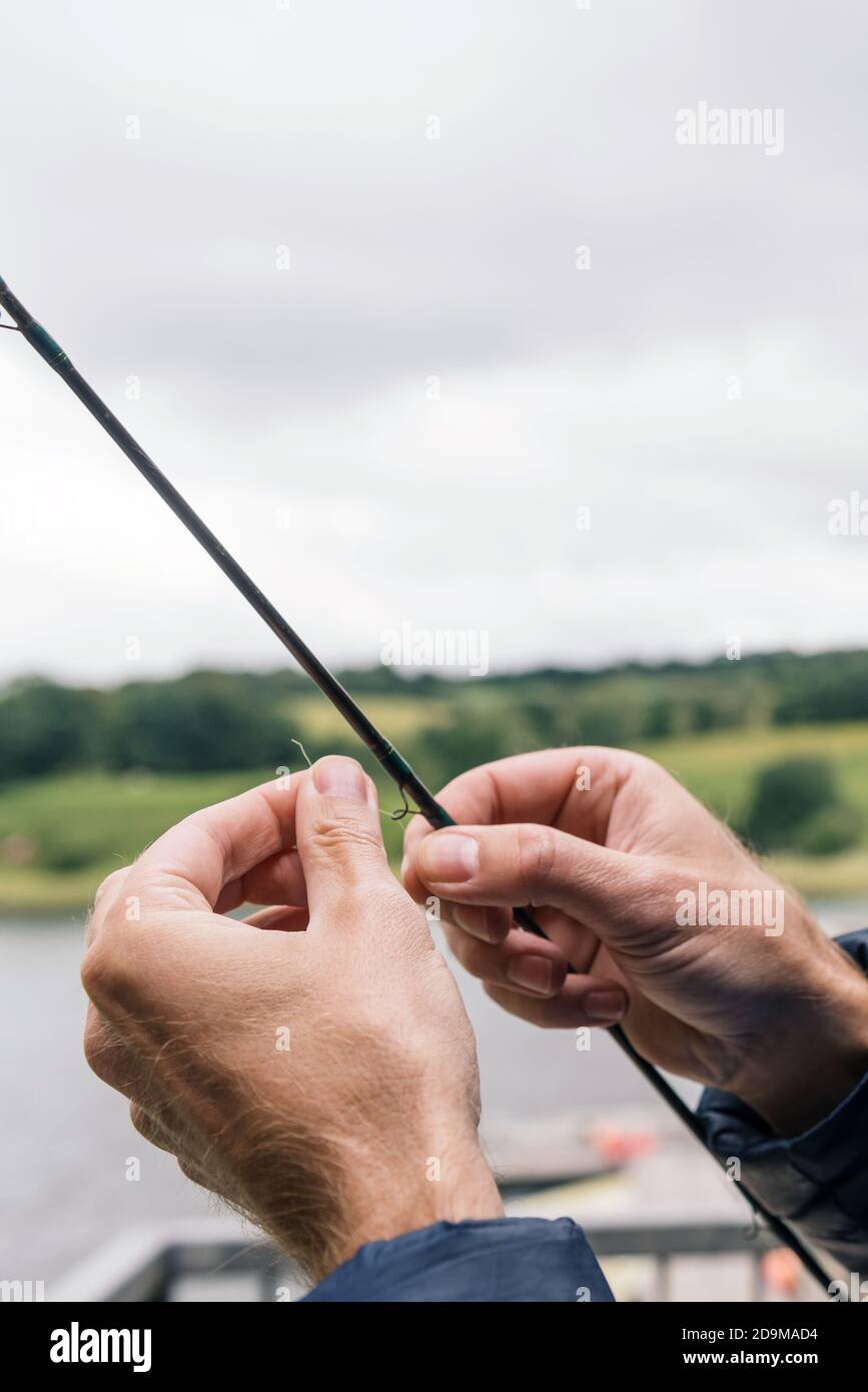 Mani maschili che mettono la lenza sulla canna da pesca Foto Stock