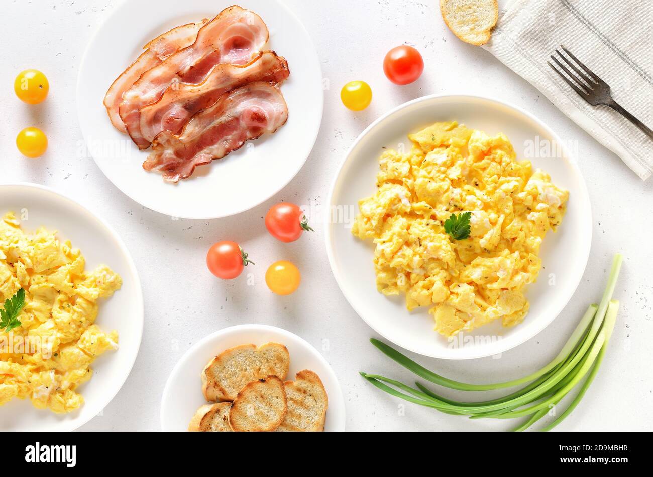 Uova strapazzate, pancetta fritta e pomodori sul piatto su fondo di pietra chiaro. Vista dall'alto, disposizione piatta Foto Stock