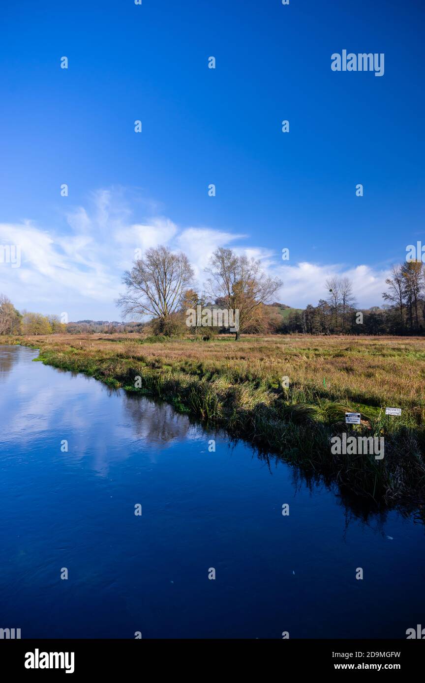 Il fiume Itchen riflette il cielo blu in un giorno di novembre soleggiato appena fuori dalla città di Winchester, in Hampshire, Inghilterra. Foto Stock