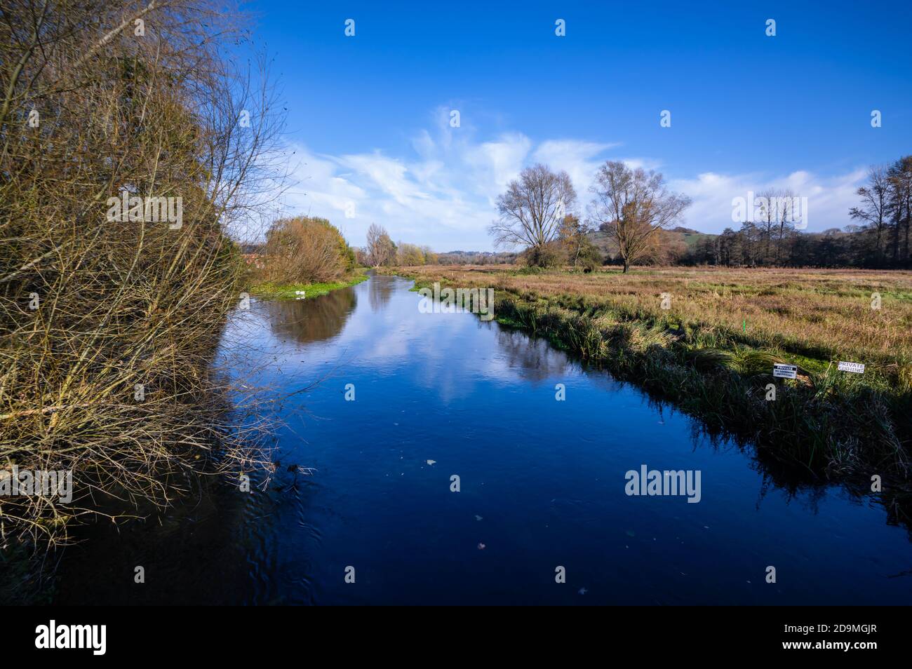 Il fiume Itchen riflette il cielo blu in un giorno di novembre soleggiato appena fuori dalla città di Winchester, in Hampshire, Inghilterra. Foto Stock