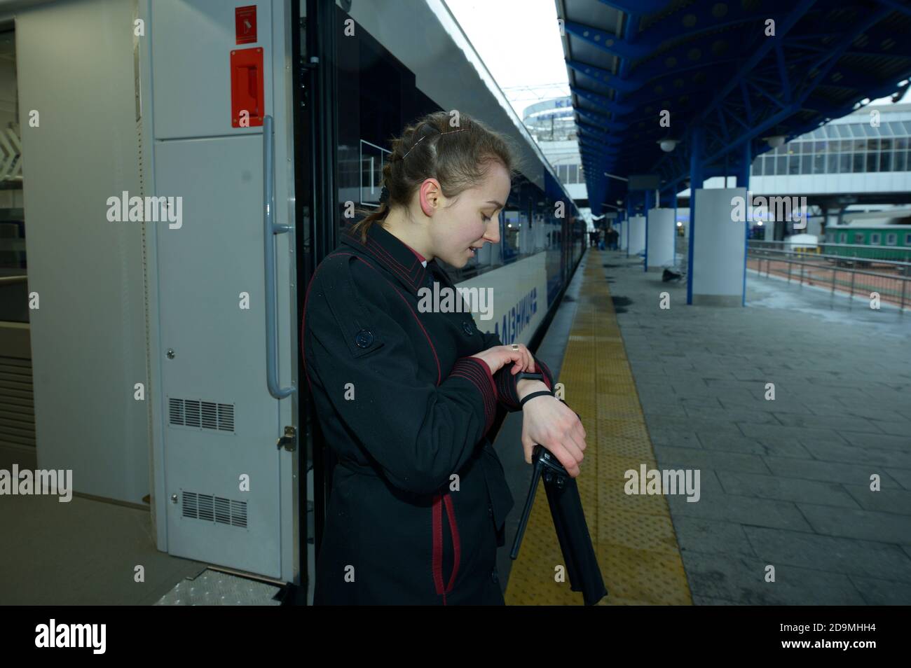 Conduttore di treno femminile che guarda il suo orologio in attesa di segnale per la partenza del treno passeggeri Foto Stock