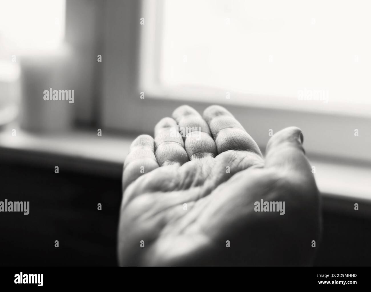 La mano umana aperta viene girata verso la finestra di giorno in giorno bianco e nero Foto Stock