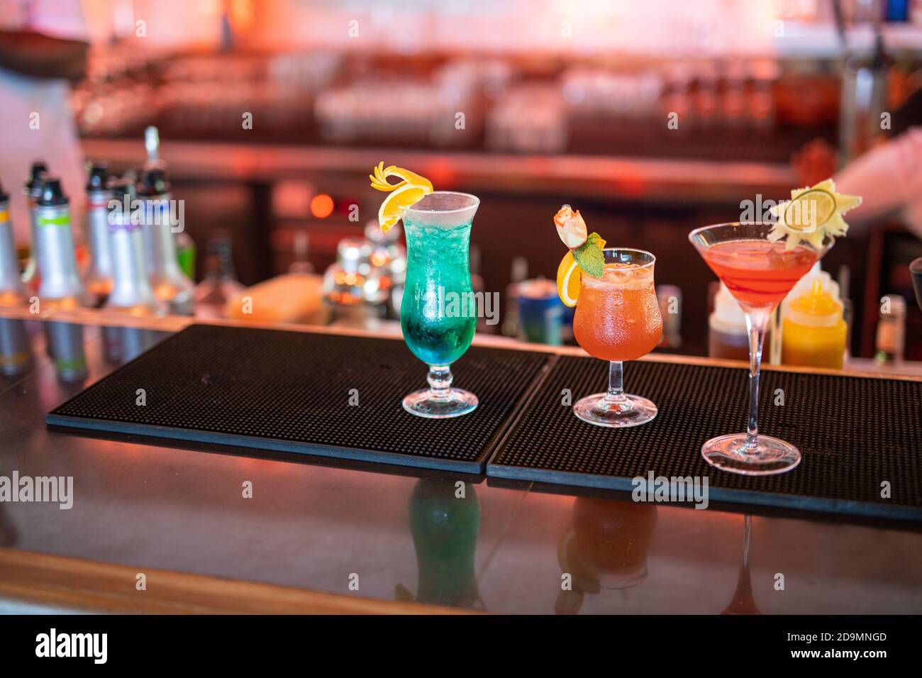 Cocktail colorati al bancone del bar. Cocktail tropicali sul tavolo del ristorante, pronti a servire. Festa della vita notturna, sottofondo di drink al bar, bottiglie sfocate Foto Stock