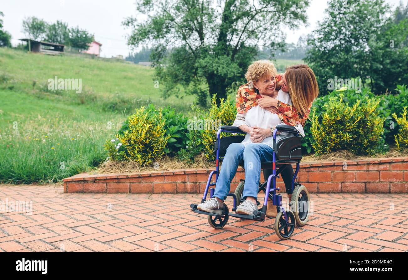 Figlia abbracciando la madre anziana in sedia a rotelle Foto Stock