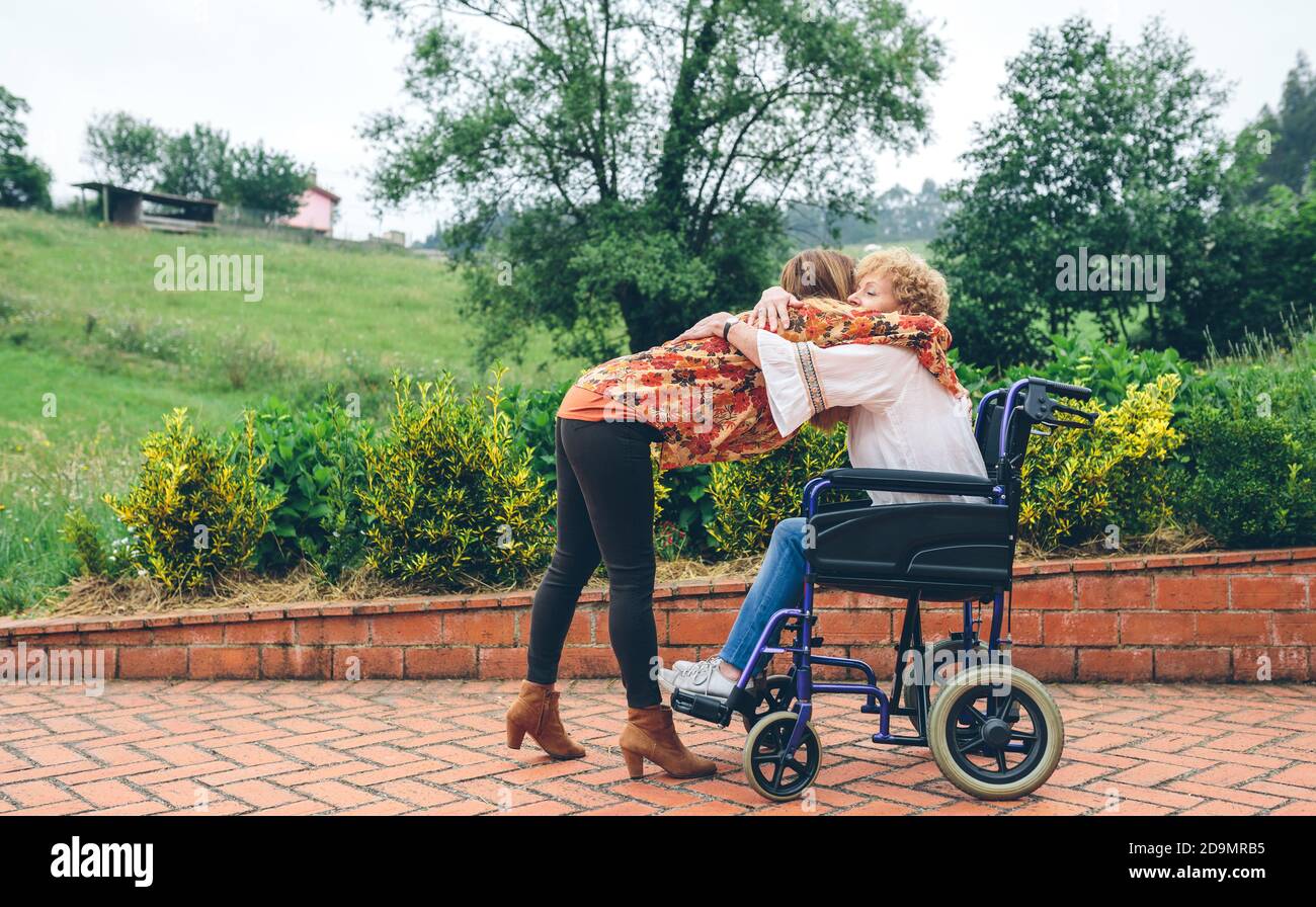 Figlia abbracciando la madre anziana in sedia a rotelle Foto Stock