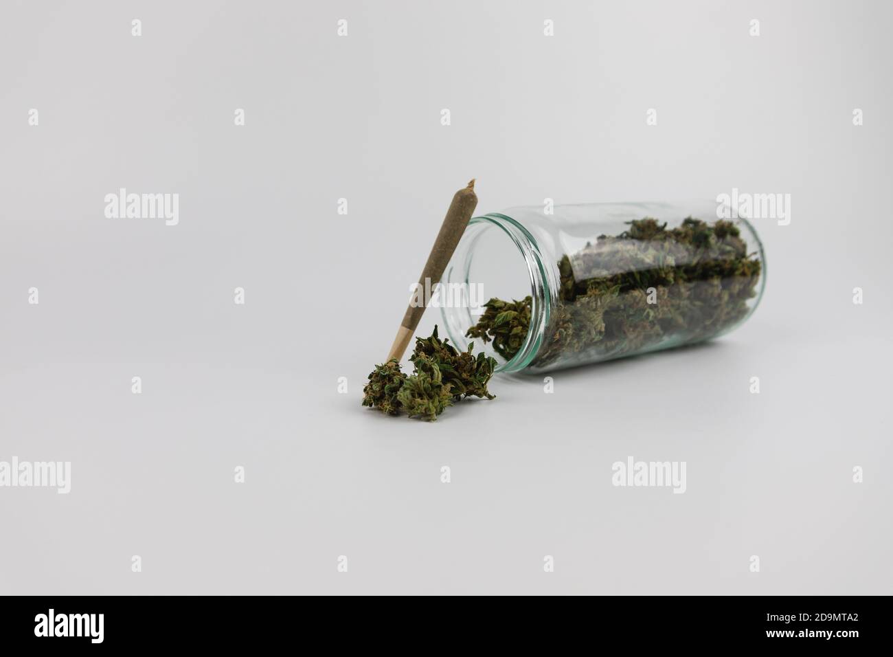 Vaso di vetro pieno di boccioli di marijuana, fiori di marijuana essiccati e una sigaretta di marijuana. Isolato su sfondo bianco. Dolce dipendenza Foto Stock