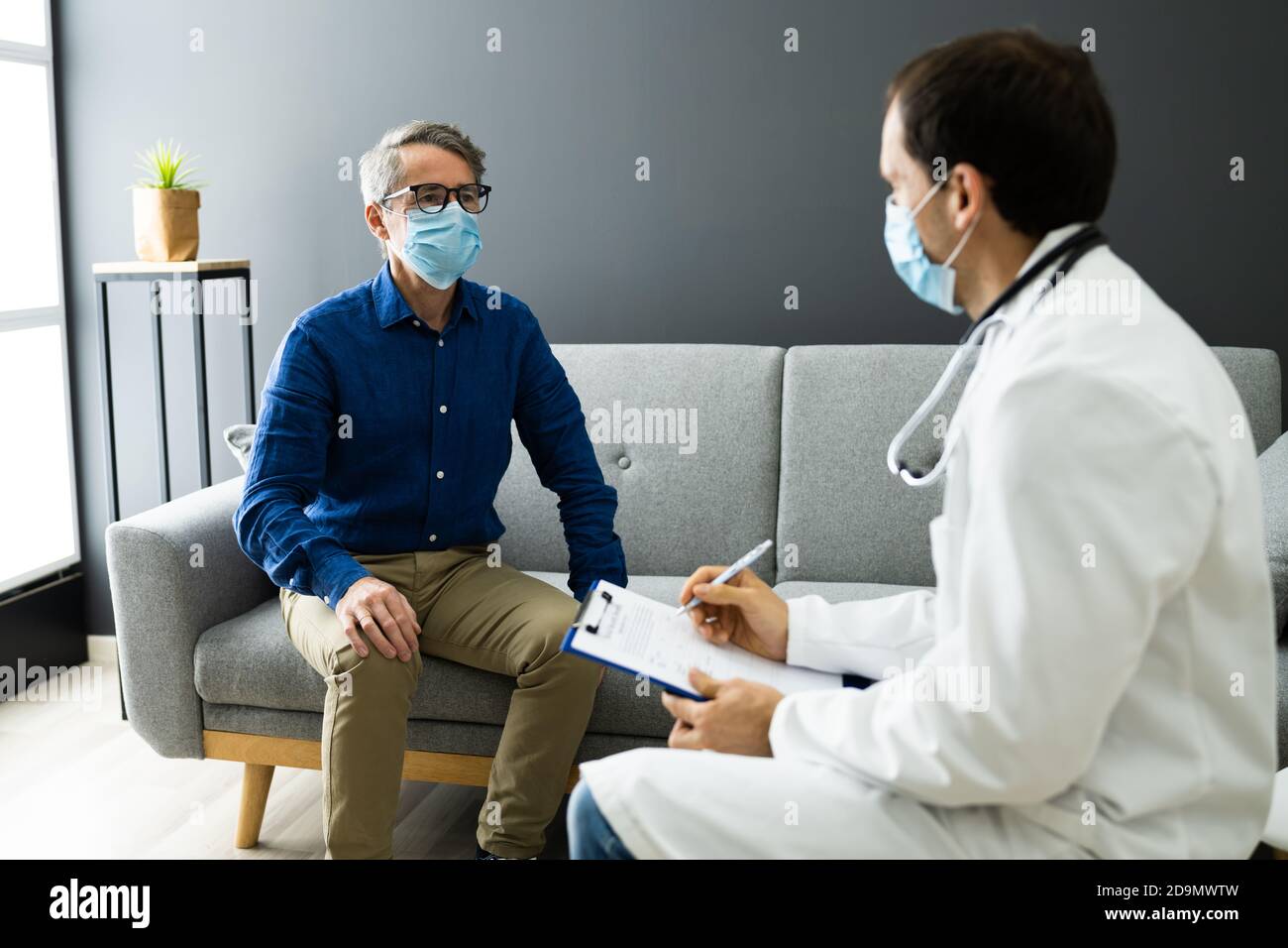 Medico con paziente anziano che vive a casa in maschera Foto Stock